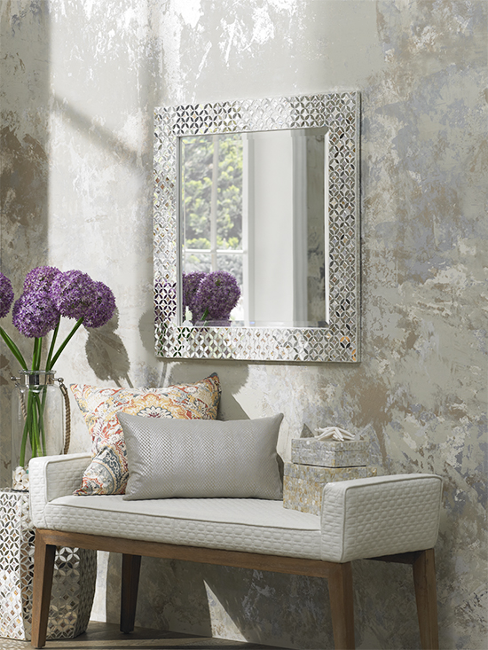 Modern chaise with wood base under a rectangular mirror in a crystal adorned frame.