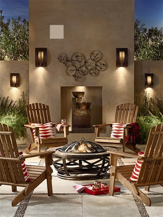 Outdoor nighttime scene with four acacia wood Adirondack chairs with red-and-white patterned pillows and an outdoor fire pit.