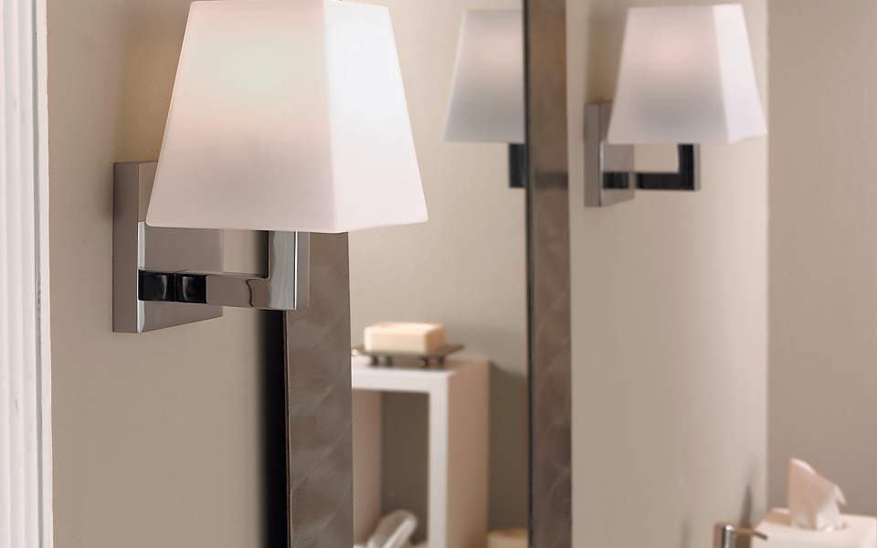 Two silver sconces topped with white shades, placed on either side of a mirror.