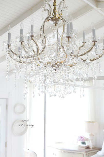 A large crystal chandelier hangs over a white themed room.