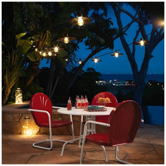 An outdoor dining set consisting of one white table and four red chairs, in a nighttime setting surrounded by glowing lights.