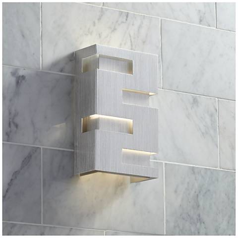 A white modern bathroom sconce, featuring a cut-out design, set against a white tiled wall.