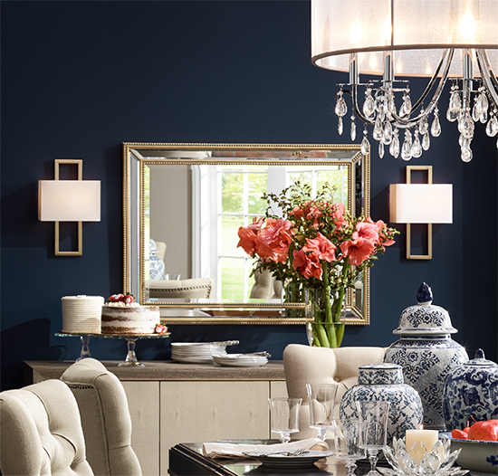 A rectangular mirror with beaded trim between two wall sconces over a sideboard. A traditional dining room with a rectangular mirror with beaded trim over a sideboard.