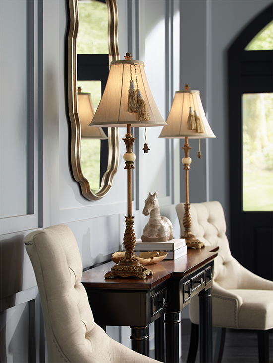 A traditional style mirror between two buffet table lamps over a sideboard.