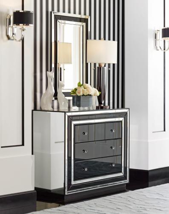 A black and white color scheme with a table lamps, mirror and dresser. 