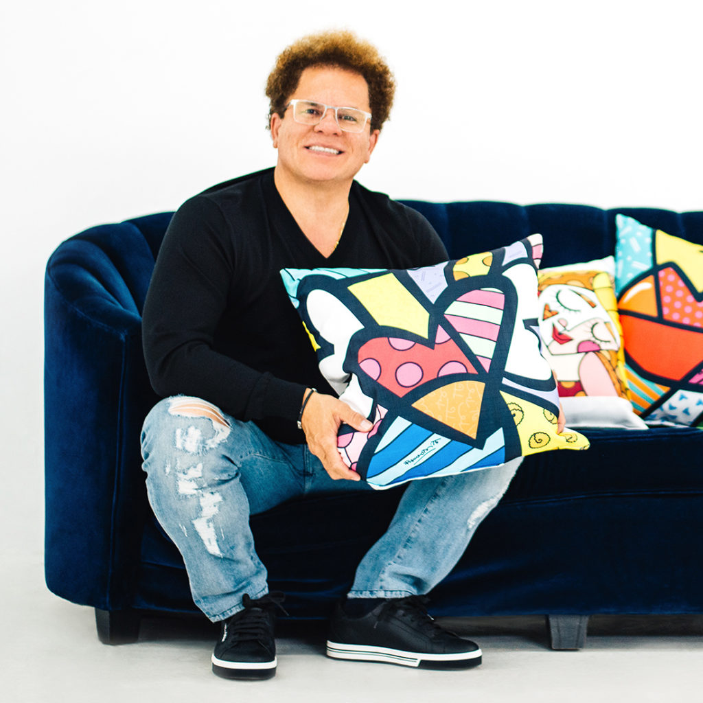Pop artist Romero Britto, sitting on a sofa with custom-print pillows